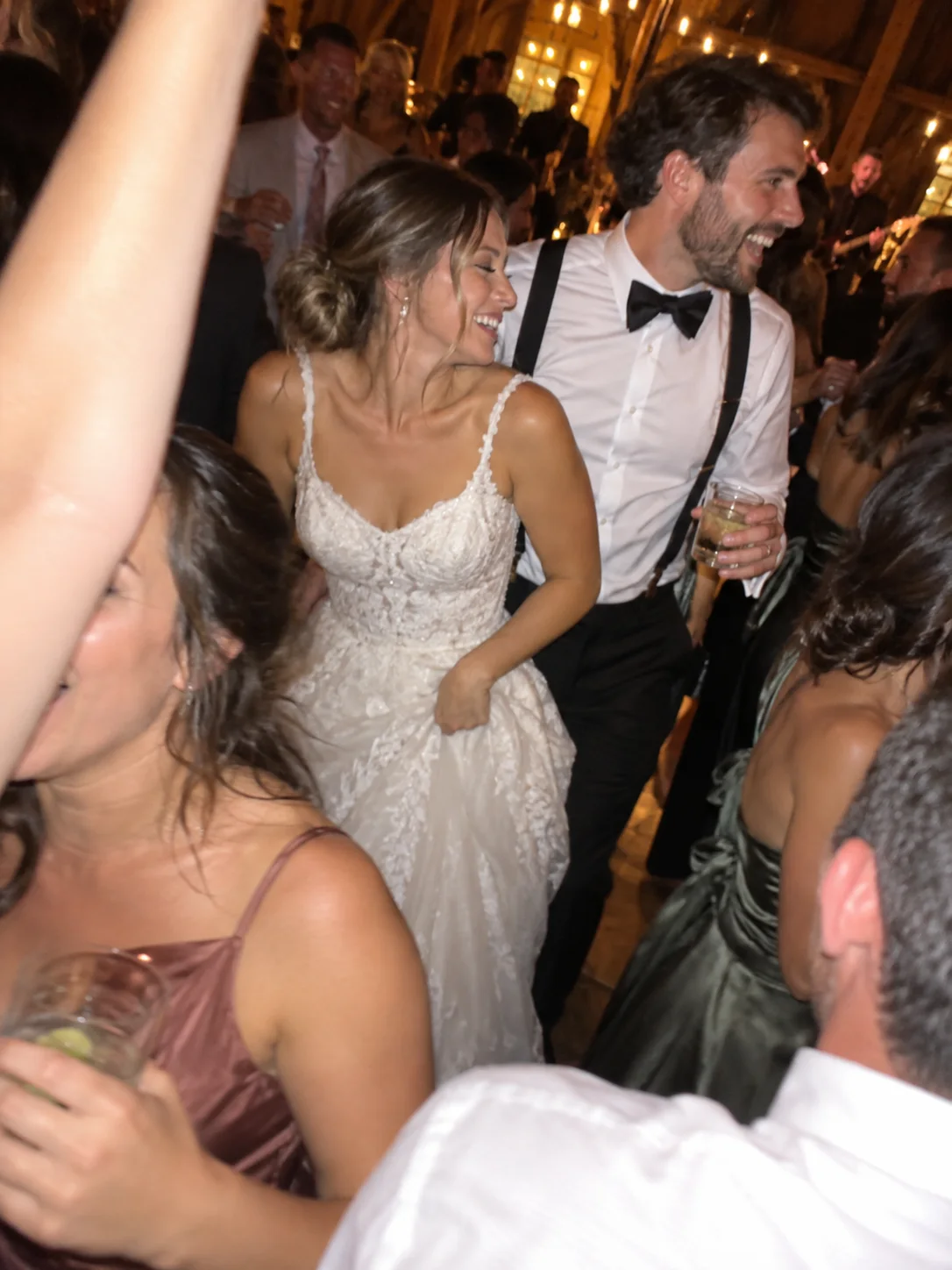 A newly married couple laughing together among guests on the dance floor